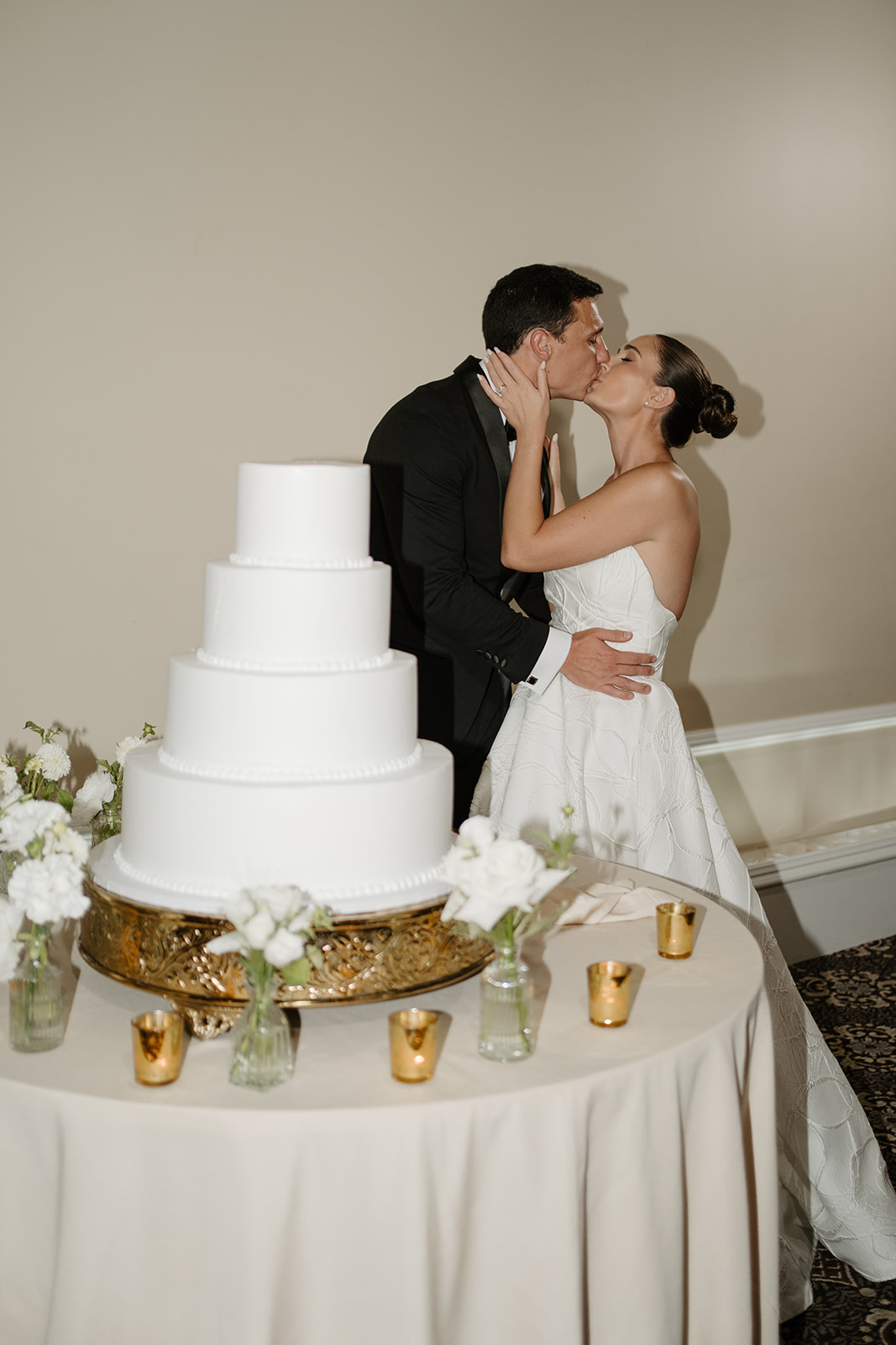 Newlyweds sharing a sweet kiss behind their four-tier white wedding cake during the reception.
